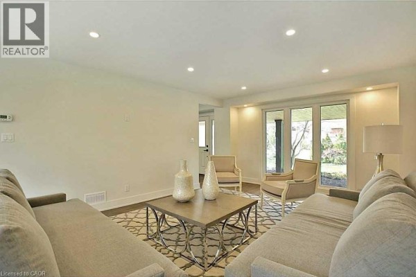 Living room with two grey sofas, two armchairs, a coffee table, and a view to the backyard. - 239 Guelph Line, Burlington