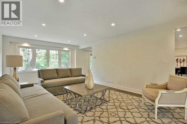 Living room with a large window overlooking trees, two grey sofas, and a decorative armchair. - 239 Guelph Line, Burlington