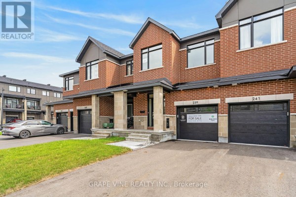 View of the townhouse exterior from the driveway showing garage doors and entranceways. - 239 Monticello Avenue, Ottawa