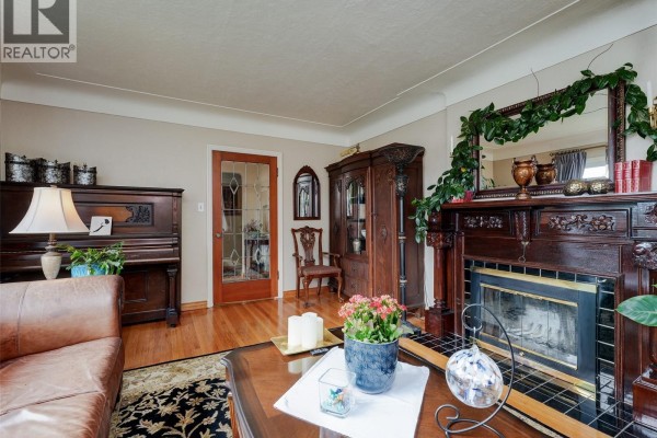 Living room with a fireplace, dark wood piano, antique china cabinet, and a glass-paned door. - 2390 Musgrave St, Oak Bay