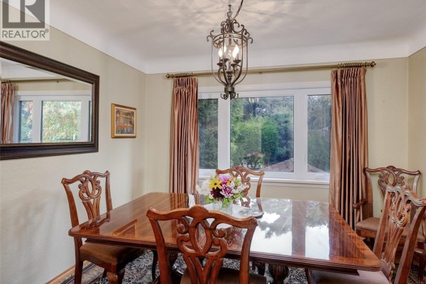 Dining room with a polished wood table and chairs, a large window, and a decorative chandelier. - 2390 Musgrave St, Oak Bay