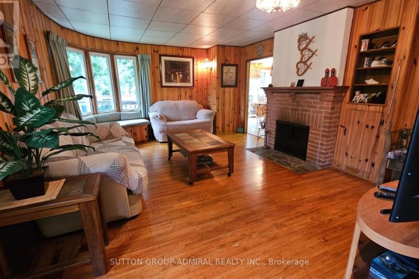 Living room with wood paneling, brick fireplace, bay window, and wood floors - 2392 Lakeshore Drive Ramara
