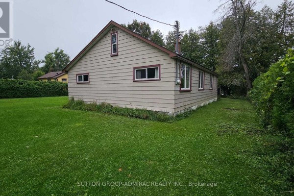 Tan vinyl-sided house with white trim windows and brick chimney - 2392 Lakeshore Drive Ramara