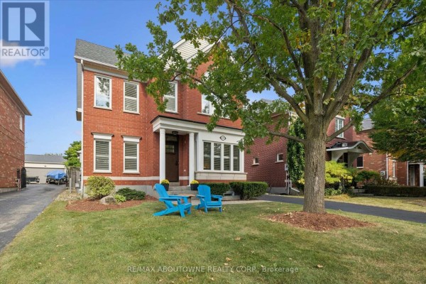 Front view of a red brick house with a large tree and two blue chairs on the lawn. - 2397 Ennerdale Road, Oakville