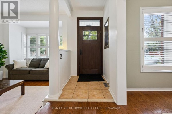 Foyer with a dark wood door, beige tile flooring, and a partial view of a living room. - 2397 Ennerdale Road, Oakville