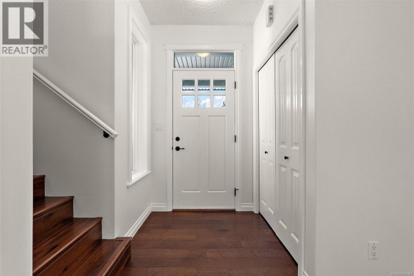 Interior entryway with white door, dark wood floor, stairs, and white walls. - 2399 Caffery Pl, Sooke