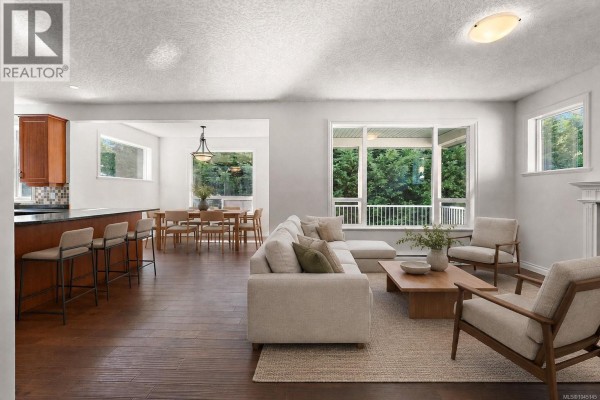 Living room with a sectional sofa, two chairs, coffee table, and view into dining room and kitchen. - 2399 Caffery Pl, Sooke