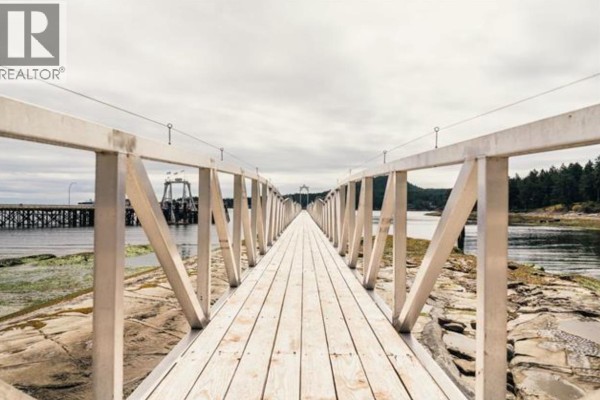 A wooden boardwalk extends over water with a cloudy sky above. - 23b 134 Madrona Road, Galiano Island