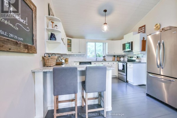 White kitchen with granite countertops, stainless steel appliances, and a breakfast bar. - 24 - 1213 Camp Jackson Road, Muskoka Lakes