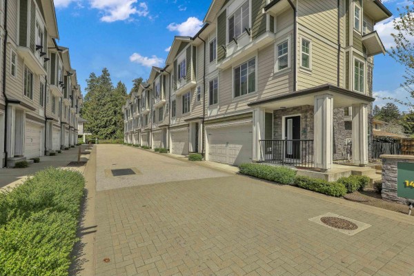 Street view of townhouses with light green and gray siding, featuring individual garages. - 24 14499 64 Avenue, Surrey