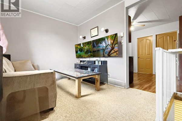 Living room with a beige sofa, a patterned coffee table, and televisions mounted on the wall. - 24 14th Avenue Se, Swift Current