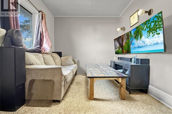 Living room with a beige sofa, a coffee table, and televisions mounted on the wall. - 24 14th Avenue Se, Swift Current