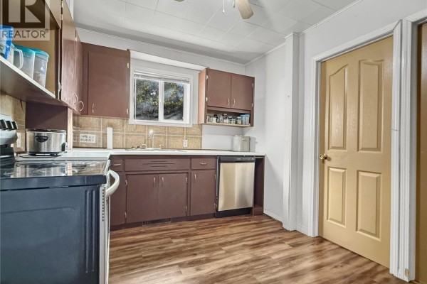 Kitchen with dark brown cabinets, stainless steel appliances, and light brown wood-look flooring. - 24 14th Avenue Se, Swift Current