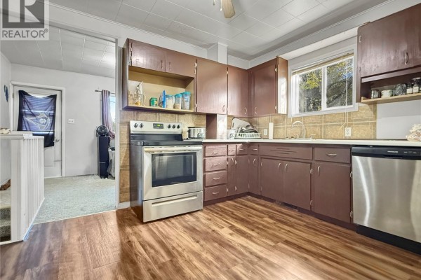 Kitchen with dark brown cabinets, a stainless steel stove, and light brown wood-look flooring. - 24 14th Avenue Se, Swift Current