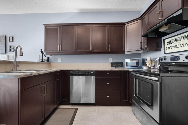 Corner kitchen with dark wood cabinets, stainless steel appliances, and light tile flooring. - #24 30 Oak Vista Dr, St  Albert