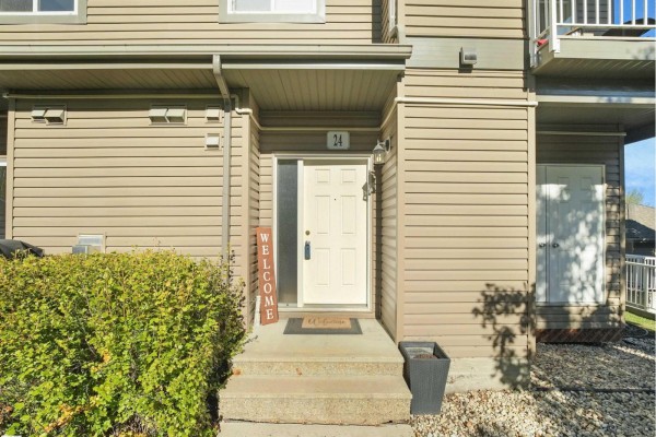 Front entrance of townhouse with beige siding, white door, and concrete steps. - #24 30 Oak Vista Dr, St  Albert
