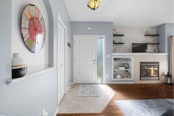 Entryway of townhouse with beige door, tile and wood flooring, and fireplace in living room. - #24 30 Oak Vista Dr, St  Albert