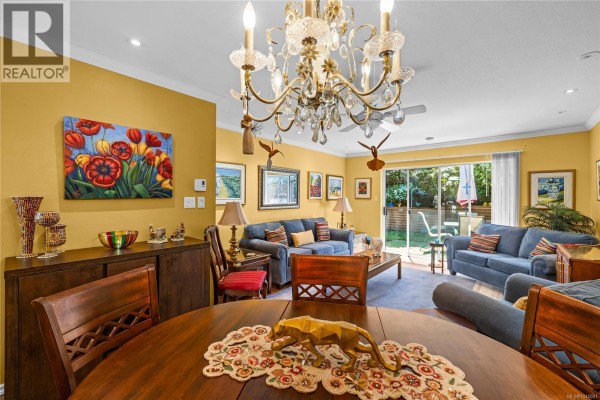 Dining area with a round wood table and chairs, adjacent to the living room with a chandelier. - 24 450 Bay Ave, Parksville