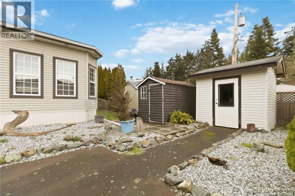 Side view of mobile home with shrubs and gravel landscaping - 24 7021 Grant Rd W, Sooke