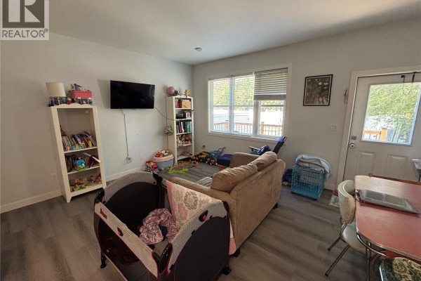 Living room with a couch, TV, shelves, and a playpen on grey flooring. - 24 A & B 2nd Avenue, Clavet