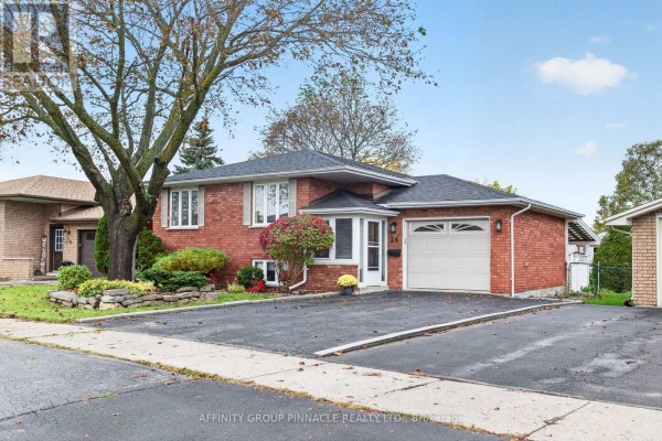 View of the red brick bungalow from the driveway with a garage and entrance. - 24 Andrew Drive, Kawartha Lakes