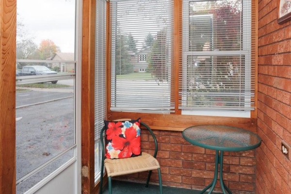 Interior sunroom with a wicker chair, table, and view of the street. - 24 Andrew Drive, Kawartha Lakes