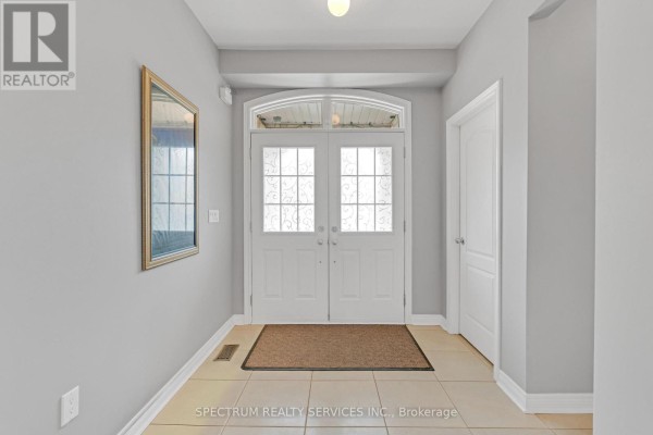 Interior entryway with beige tile floor, grey walls, double white doors, and a large gold framed mirror. - 24 Aristocrat Road, Brampton