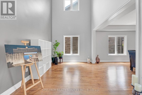 Spacious living room with vaulted ceiling, hardwood floors, large windows, and an easel with artwork. - 24 Aristocrat Road, Brampton