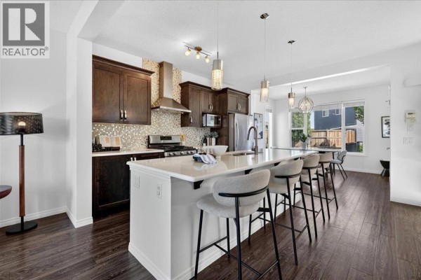 A spacious kitchen with dark wood cabinets, a large island with pendant lights, and stainless steel appliances. - 24 Auburn Meadows Green Se, Calgary