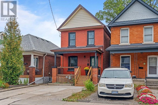 Front facade of a red brick house with dark trim, a porch, and blooming flowers. - 24 Belview Avenue, Hamilton