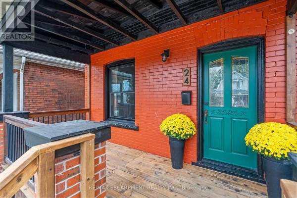 Close-up of a covered porch with red brick walls, a green door, and yellow flowers. - 24 Belview Avenue, Hamilton