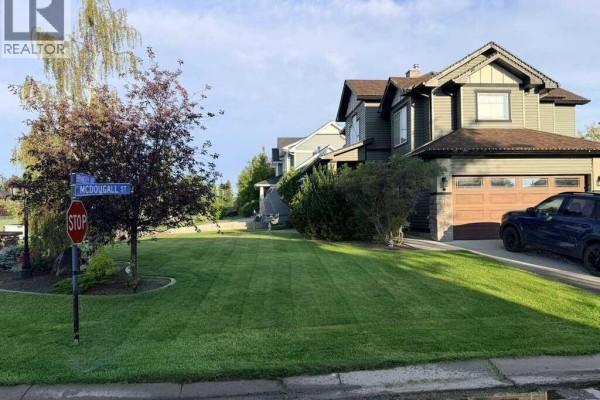 Street view showing a manicured lawn, double garage, and the side of the house. - 24 Brander Avenue Nw, Langdon