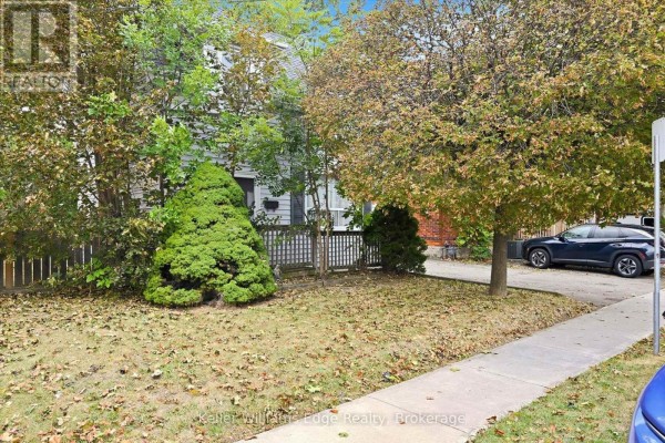 Front yard with grass, trees, and a sidewalk in front of the house. - 24 Brucedale Avenue W, Hamilton