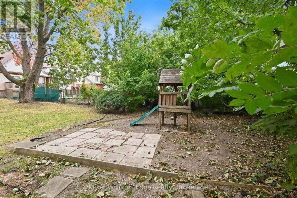 Backyard with a play structure, slide, and paved patio surrounded by trees. - 24 Brucedale Avenue W, Hamilton