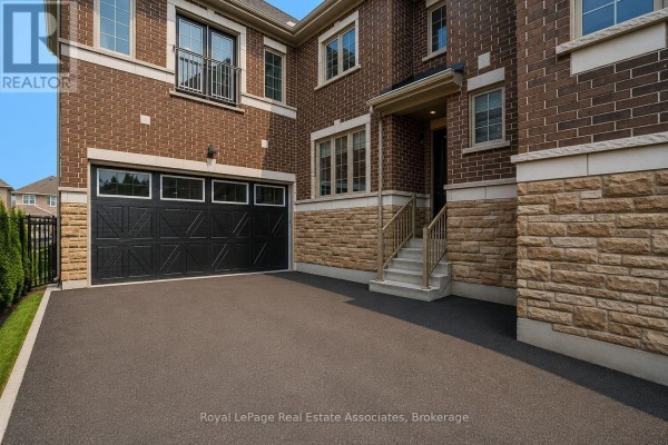 Close-up of the attached garage door, stone facade, and entry stairs to the brick house. - 24 Burke Street, New Tecumseth