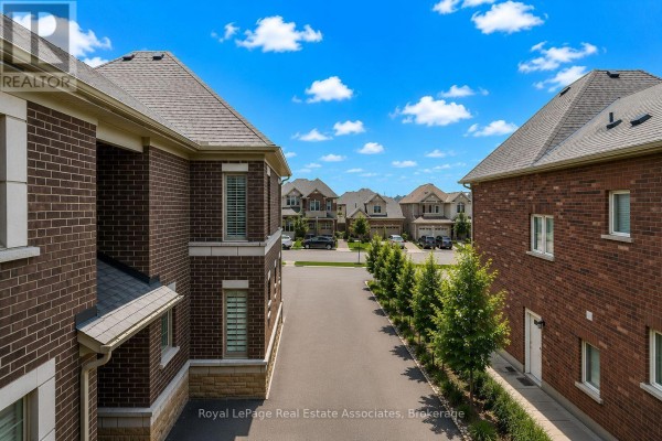 View down a paved driveway lined with trees, between two brick houses with suburban homes in the distance. - 24 Burke Street, New Tecumseth