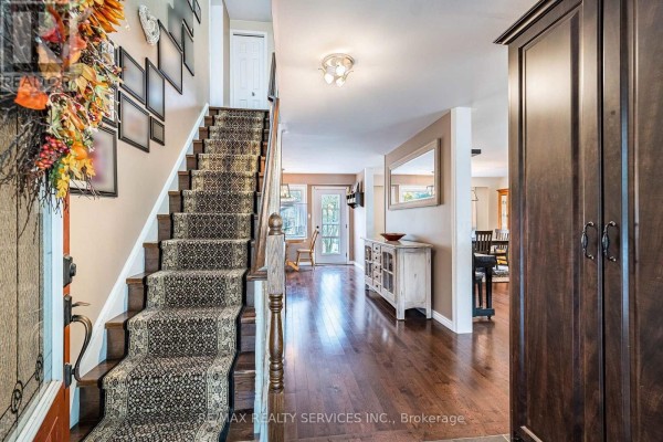 Interior view of a foyer with a carpeted staircase, hardwood floors, and dark wood cabinetry. - 24 Carberry Road Street, Erin
