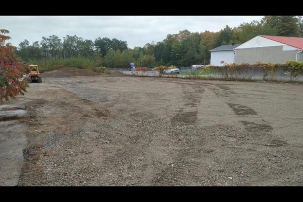 Wide view of an undeveloped industrial lot with trees and buildings in background. - 24 Commerce Park Drive, Innisfil