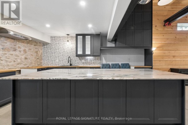 Kitchen island with a marble countertop facing dark grey cabinets and a stone accent wall. - 24 Davidson Street, Cambridge