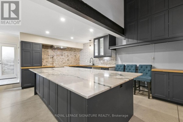 Open concept kitchen with a large grey island, dark grey cabinets, and a stone wall. - 24 Davidson Street, Cambridge