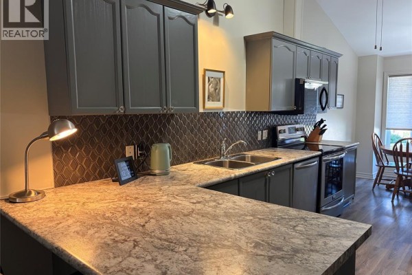 Kitchen with dark gray cabinets, a gray backsplash, and a light-colored countertop. - 24 Erie Glen Crescent, Leamington