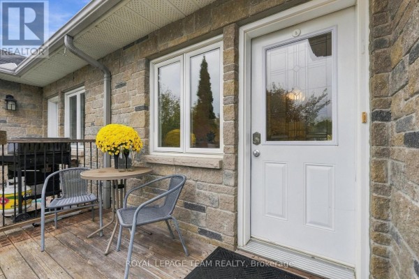 Wooden deck with two chairs and a small table outside the front entrance. - 24 Farm Street, Mississippi Mills