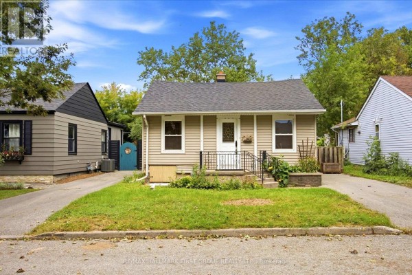 Side exterior view of a beige bungalow with a tree in the front yard and a paved driveway. - 24 George Street, Ajax