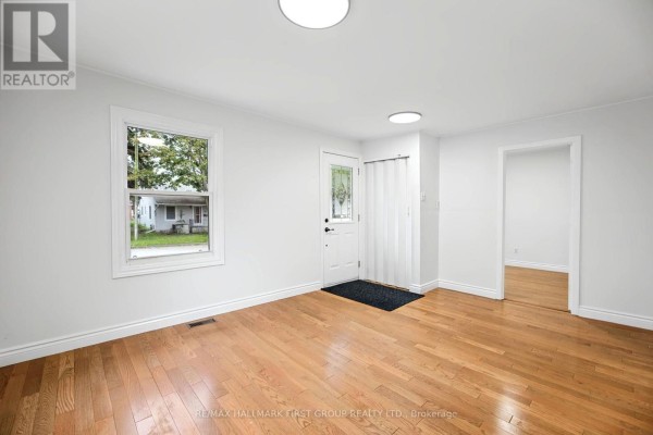 Spacious living room with hardwood floors, light green walls, and access to a hallway. - 24 George Street, Ajax