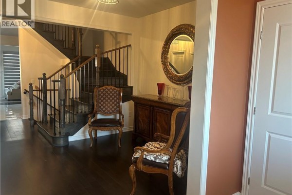 Foyer with dark hardwood floors, a wooden staircase with black railings, and two accent chairs. - 24 Heming Trail, Ancaster