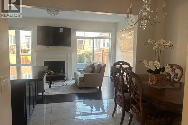 Living room with a fireplace, armchair, and a large window overlooking a backyard patio. - 24 Heming Trail, Ancaster