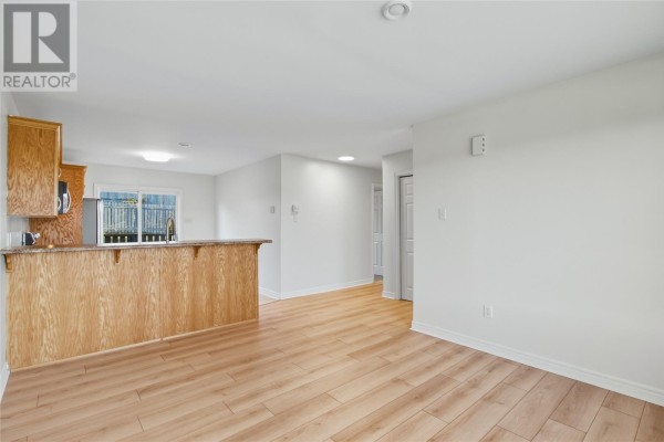 Open concept living area with kitchen island, light wood laminate flooring, and white walls. - 24 Hopedale Crescent, St  John S