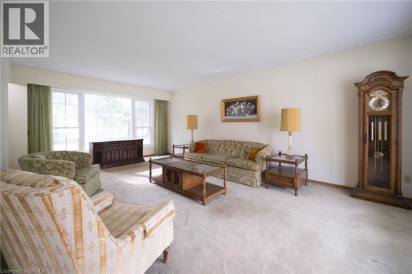 Spacious living room with beige carpet, large windows, sofas, armchairs, and a grandfather clock. - 24 Japonica Crescent, Brantford