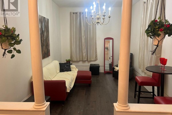 Living room with a cream sofa, red accent chairs, dark hardwood floors, and a chandelier. - 24 King Street W, Kawartha Lakes