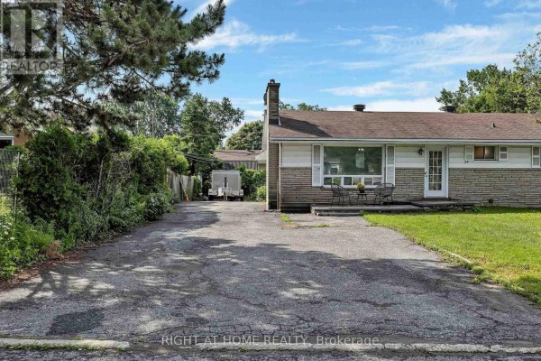 Side view of the house and driveway with dense greenery on the left and a trailer in the background. - 24 Largo Crescent S, Ottawa